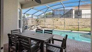 Ein überdachter Patio-Bereich mit Pool, Gartenmöbeln und Deckenventilator.
