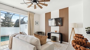 Una sala de estar moderna con sofá, sillones, televisor y vista a la piscina.