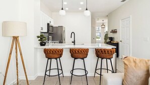 Una cocina moderna con una isla blanca, taburetes negros y lámparas colgantes.