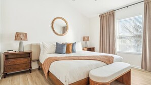 Un dormitorio con cama, mesitas de noche, un espejo redondo y una ventana con cortinas.