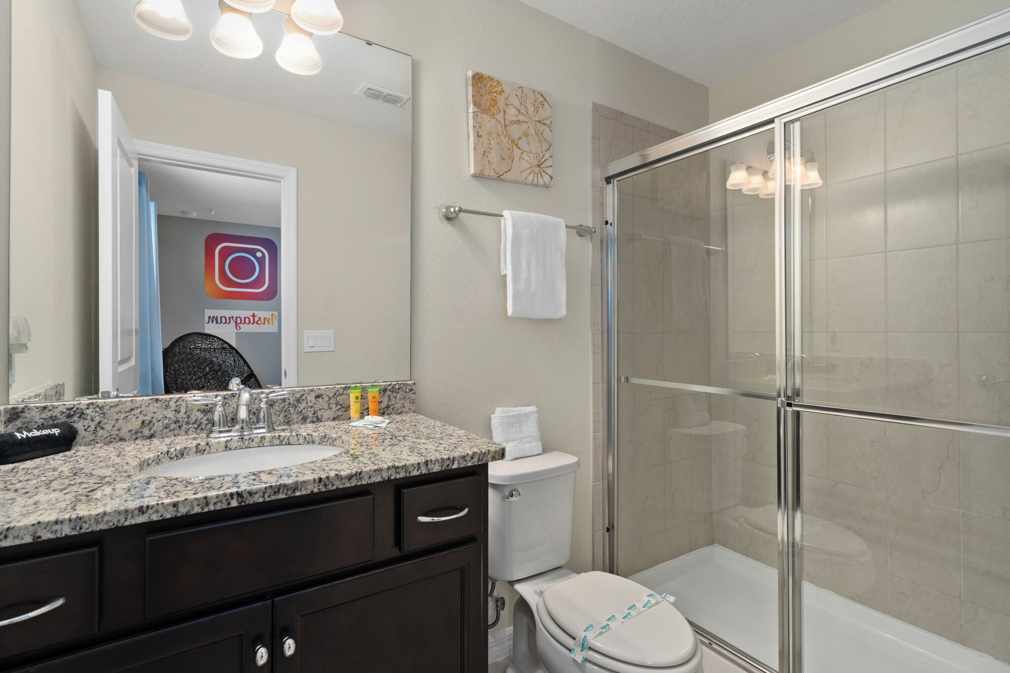 A modern bathroom with a granite countertop, a toilet, a glass-enclosed shower, and a towel rack.