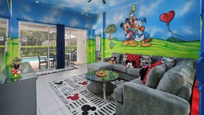 Ein Wohnzimmer mit einer großen Wandmalerei von Mickey Mouse, grauen Sofas, einem Couchtisch und Blick ins Freie.