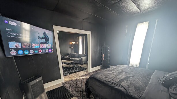 Ein modernes Hotelzimmer mit einem großen Bett, einem Fernseher, der 'Predator: Badlands' zeigt, und einer Sitzecke mit Sofa und Couchtisch.