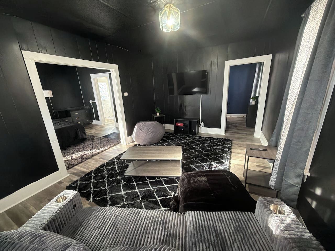 A modern room with a black and white color scheme, a flat-screen TV mounted on the wall, and a large mirror reflecting the room.