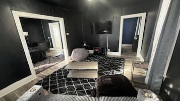 A modern room with a black and white color scheme, a flat-screen TV mounted on the wall, and a large mirror reflecting the room.
