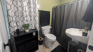 Ein Badezimmer mit Toilette, Waschbecken, Duschvorhang und einem schwarzen Regal mit einer Pflanze.