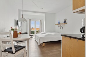 A modern room with a bed, a dining table, a chair, a hanging light, and a kitchen area. - Pension Koch, apartment 6 (Gudhjem)