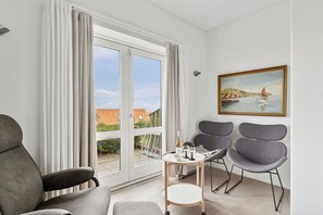 A modern room with a large window, a painting, and a table with a bottle and glasses. - Pension Koch, apartment 6 (Gudhjem)
