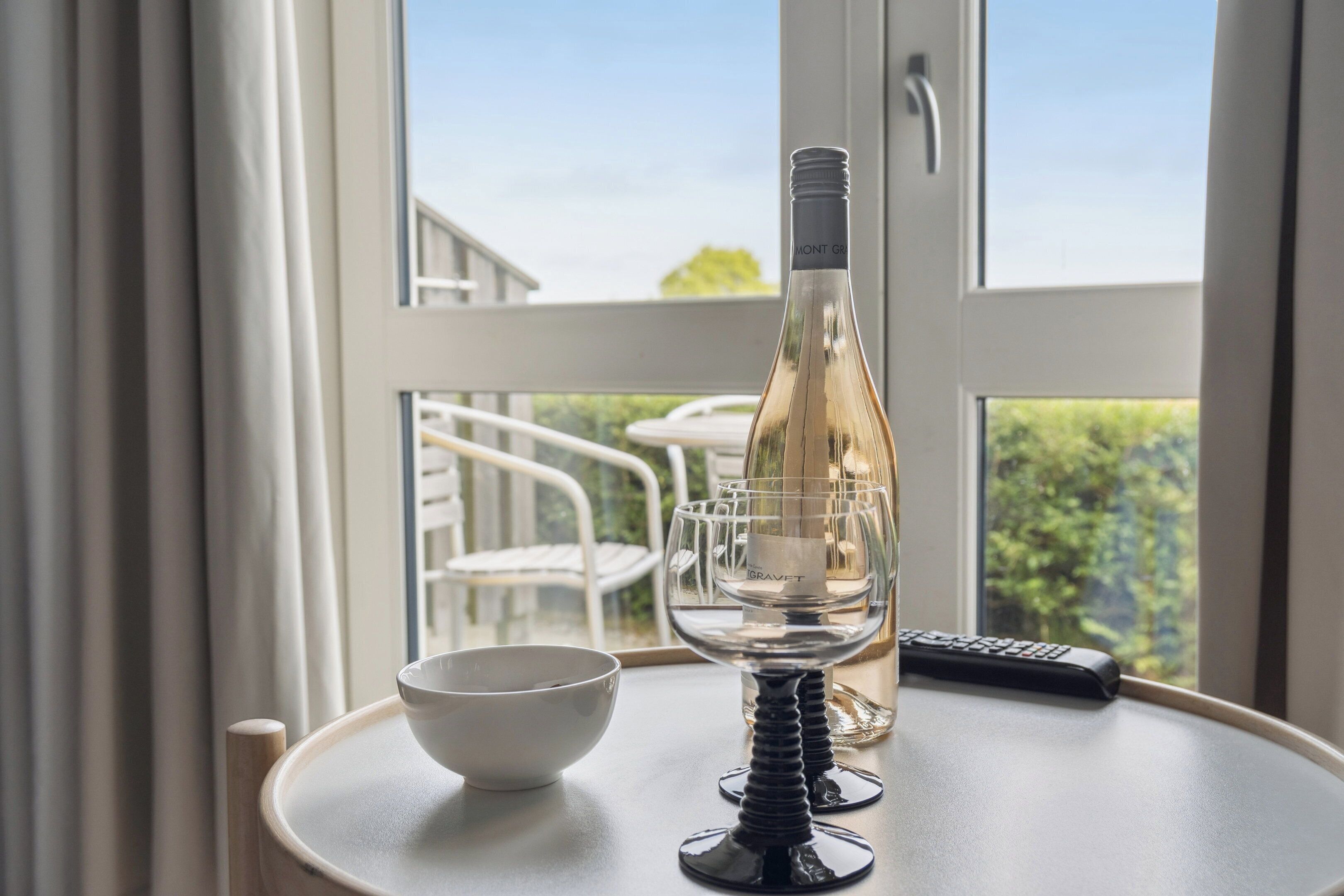 A table with a wine bottle, a glass, and a remote control.