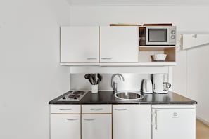 A compact kitchen with white cabinets, a microwave, a coffee maker, and a sink. - Pension Koch, apartment 6 (Gudhjem)