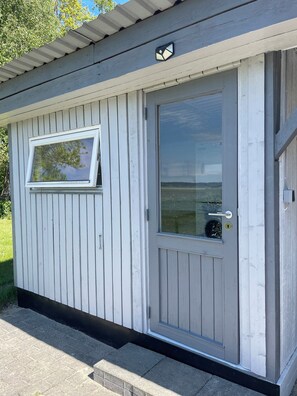 A small, single-story building with a white exterior, a sliding glass door, and a window. - Peaceful holiday home with views of Randers Fjord (Ørsted)