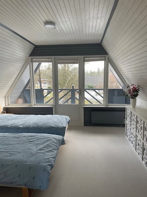 A bedroom with a sloped ceiling, a bed with a patterned duvet, a radiator, and a window with a view of the outside. - Peaceful holiday home with views of Randers Fjord (Ørsted)