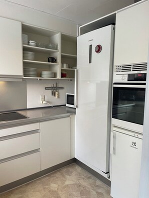 A modern kitchen with white cabinets, a built-in microwave, a refrigerator with a digital display, and a tiled backsplash. - Peaceful holiday home with views of Randers Fjord (Ørsted)