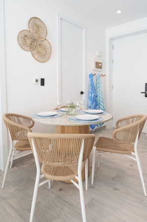 A dining area with a round table, four wicker chairs, and a wall-mounted decorative item. - Chic Tropical 1 BD APT near Downtown Punta Cana with AC and gym (Punta Cana)