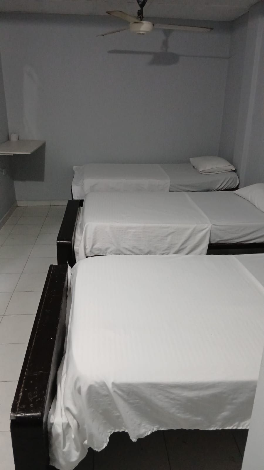 Una habitación con tres camas individuales, un ventilador de techo y una mesita con una taza.
