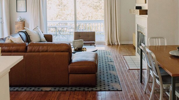 Un salon moderne avec un canapé en cuir marron, une table à manger avec des chaises et une grande fenêtre avec des rideaux.