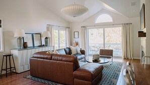 Un salon spacieux avec un canapé en cuir marron, une table basse ronde et une grande fenêtre avec des rideaux.
