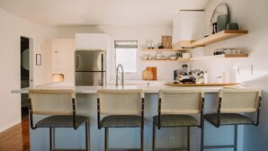 Une cuisine moderne dotée d’un îlot central, de tabourets de bar, d’un réfrigérateur et d’étagères intégrées.