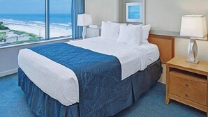 Ein Hotelzimmer mit einem großen Bett, einem Nachttisch, einer Lampe und Blick auf den Strand.