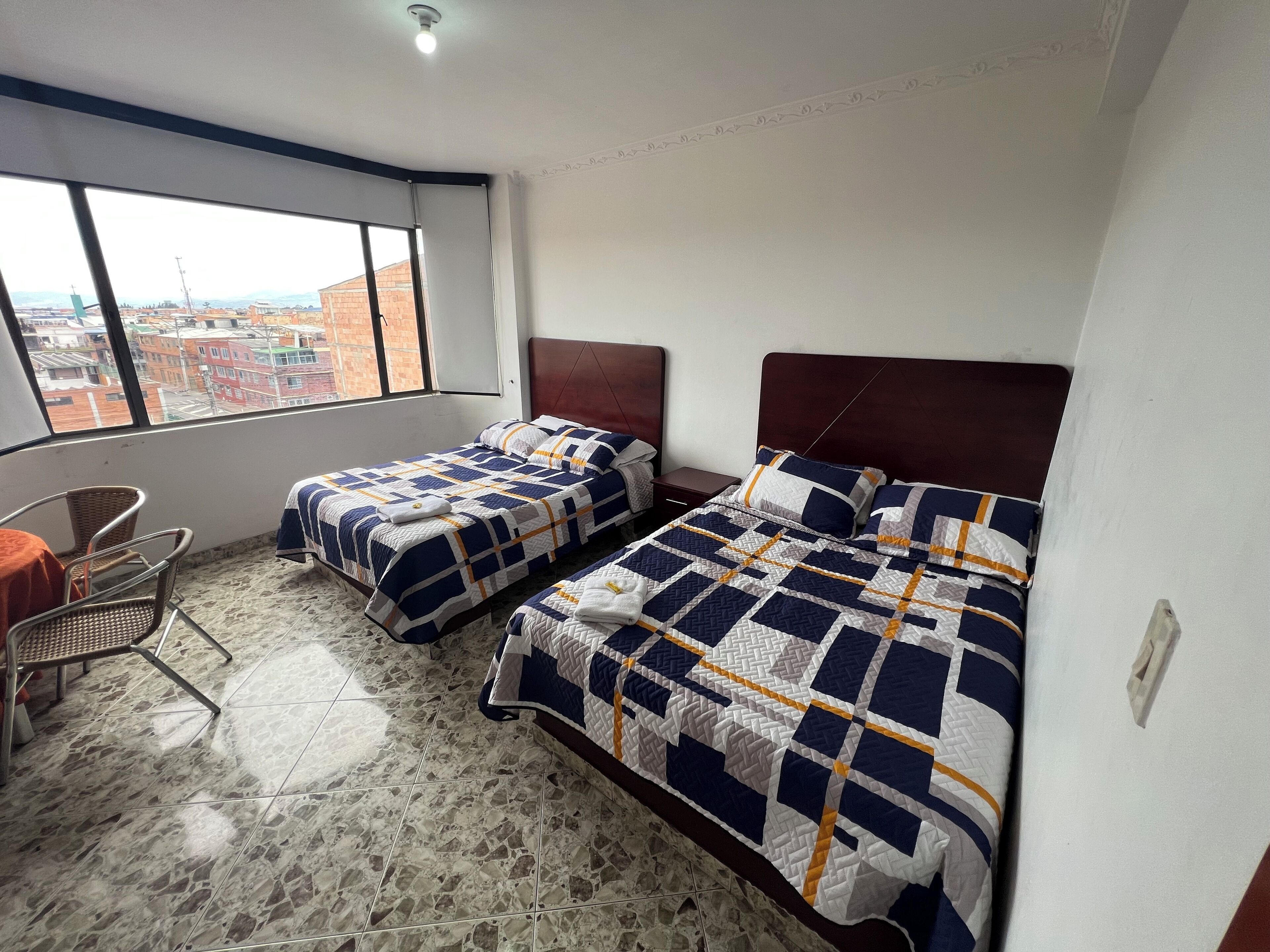 Habitación de hotel con dos camas, una silla y vista a la ciudad.