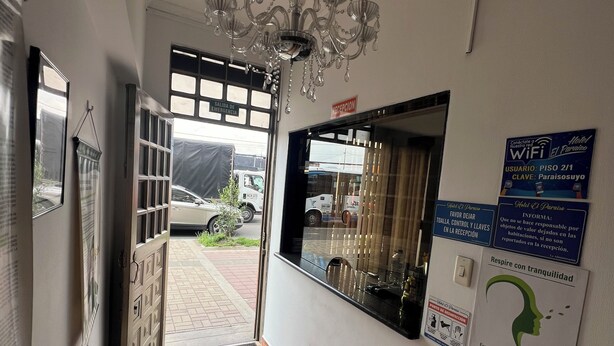 A hotel reception area with a chandelier, a reception desk, and a view of the outside. - Hotel El paraíso Funza  (Funza)