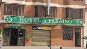 A multi-story building with a green sign for Hotel El Paraiso 24, featuring a restaurant and a closed shuttered storefront. - Hotel El paraíso Funza  (Funza)