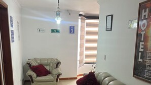 A hotel lobby with a beige leather sofa, a smaller armchair, and a chandelier. There are signs indicating room numbers and a 'HOTEL' sign on the wall. - Hotel El paraíso Funza  (Funza)