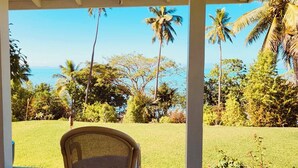 A covered outdoor area with a wicker chair, palm trees, and a view of the ocean. - Beachfront Retreat at Rainbow Reef (Savusavu)
