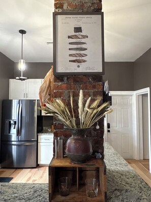 A kitchen with a brick wall, a framed patent office certificate, a vase with dried plants, and a stainless steel refrigerator. - Cozy 2-bedroom pet friendly Historic Old Cigar House (Tampa)