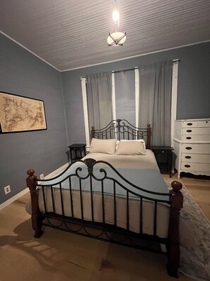 Quarto com cama, mesa de cabeceira, cômoda, mapa na parede e luminária no teto.