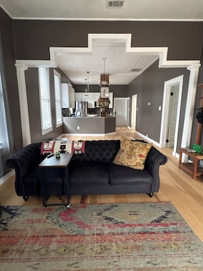 A modern living room with a black leather sofa, a patterned rug, and a kitchen in the background. - Cozy 2-bedroom pet friendly Historic Old Cigar House (Tampa)