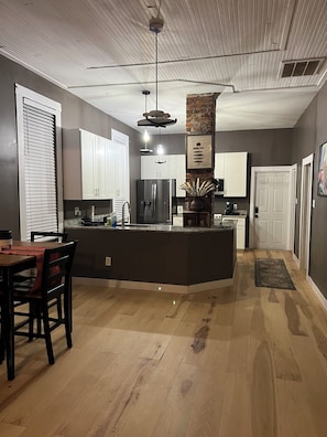 A modern kitchen with a central island, white cabinets, and a dining area with a table and chairs. - Cozy 2-bedroom pet friendly Historic Old Cigar House (Tampa)
