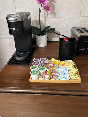 A kitchen counter with a Keurig coffee maker, a toaster, a potted plant, and a tray of coffee pods and sugar packets.