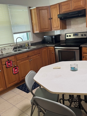 A kitchen with wooden cabinets, a microwave, an oven, a sink, and a dining table with chairs.