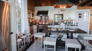 A kitchen with white cabinets, a central island with stools, a large stove, and a hanging light fixture. - Storybook family cottage perched atop Penn Cove (coupeville)