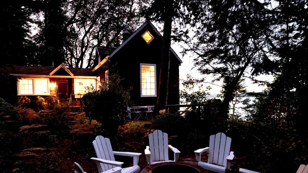 A cabin with a fire pit and white chairs in the yard. - Storybook family cottage perched atop Penn Cove (coupeville)