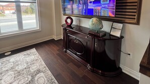 Uma sala de estar com uma grande TV de tela plana presa na parede, um móvel de entretenimento de madeira escura abaixo e um tapete estampado no chão.