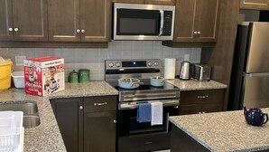 Uma cozinha moderna com armários de madeira escura, micro-ondas de aço inoxidável, forno Samsung, bancadas de granito e geladeira de aço inoxidável.