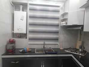 Eine moderne Küche mit Gasherd, Spüle und einem Fenster mit horizontalen Jalousien.