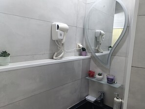 Ein Badezimmer mit einem weißen Waschbecken, einem Spiegel, einem Fön und einem Regal mit einer Topfpflanze.