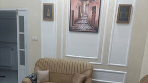 A living room with a beige sofa, a coffee table, and a rug. There are framed pictures on the wall and a door to the left. - COMFORT in the heart of Algiers (Alger Centre)