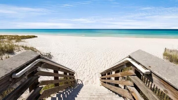 Una escalera de madera que conduce a una playa con vistas claras al océano.