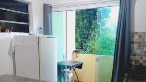 Une cuisine dotée d’un plan de travail en granit, d’un réfrigérateur, d’une fenêtre avec des rideaux et offrant une vue sur la verdure à l’extérieur.
