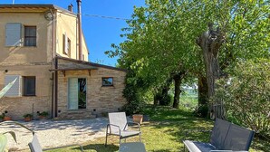 A two-story building with a stone facade, a small front porch, and a grassy yard with a bench. - Lovely home in Mombaroccio (Mombaroccio)