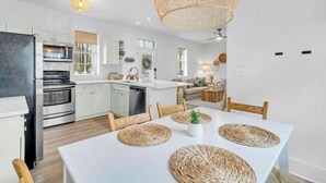 A modern kitchen with white cabinets, stainless steel appliances, and a dining area with a white table and woven placemats. - The Blue Bungalow by Stay on 30a (Seagrove Beach)