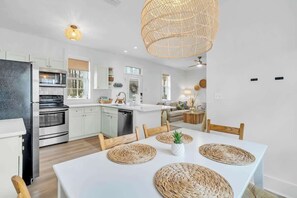 Une cuisine moderne avec des meubles blancs, des appareils en acier inoxydable et un coin repas comprenant une table blanche et des sets de table en fibres tressées.
