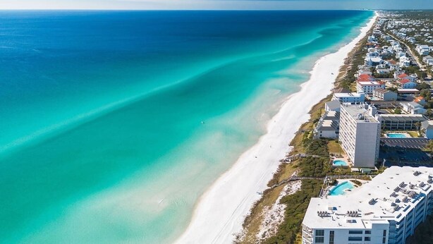 An aerial view of a coastal area with a beach, buildings, and a hotel with a pool. - The Blue Bungalow by Stay on 30a (Seagrove Beach)