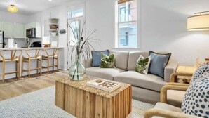 A modern living room with a sofa, coffee table, and chairs. There is a kitchen area with cabinets and a microwave. - The Blue Bungalow by Stay on 30a (Seagrove Beach)