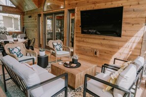 A wooden cabin interior with a dining area, wicker furniture, a coffee table, and a large window. - Lake Ida+Fish+Foosball+Bball+PingPong+Fire+Porch (Alexandria)