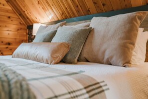 Een houten cabin met een bed, kussens en een lamp.